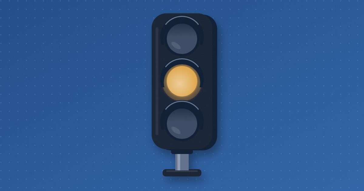 A traffic light on a short pole with its top and bottom lamps dark and only the middle lamp lit in amber.